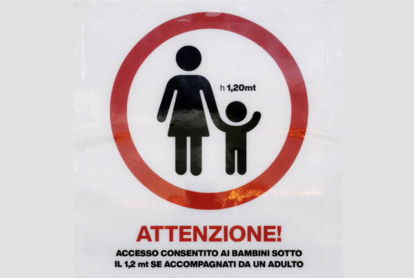 Cartello fuori da una toilette che raffigura una donna stilizzata che tiene per mano un bambino. Il testo recita: Attenzione! Accesso consentito ai bambini sotto il 1,2 mt se accompagnati da un adulto.